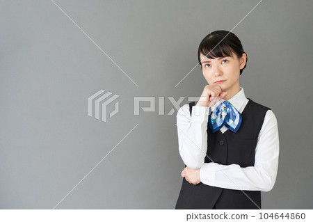 一位從事接待工作和文書工作的女性，身穿制服，背心上繫著絲帶，做出思考的手勢 104644860