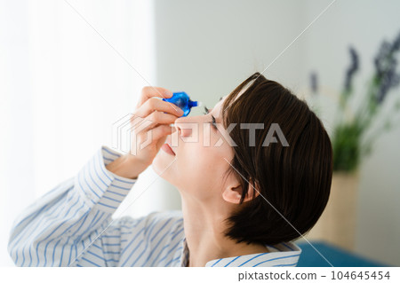 Young woman taking eye drops hay fever image Young woman taking eye drops hay fever image 104645454