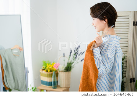 Fashion image of a young woman choosing clothes in front of a mirror 104645465