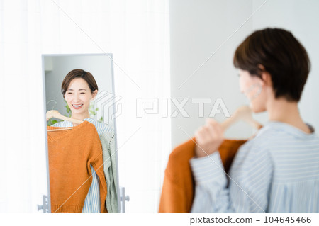 Fashion image of a young woman choosing clothes in front of a mirror 104645466
