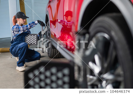 A female auto mechanic makes a camber. Woman working in a car service. A female auto mechanic makes a camber. Woman working in a car service. 104646374