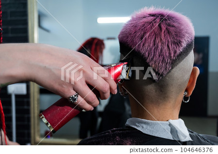 The hairdresser shaves the temple of a female client. Rear view of a woman with short pink hair in a barbershop. 104646376