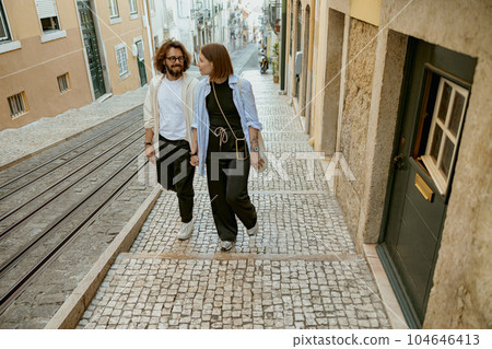 Beautiful hipster couple in love walking on old city street in Lisbon in a good mood Beautiful hipster couple in love walking on old city street in Lisbon in a good mood 104646413