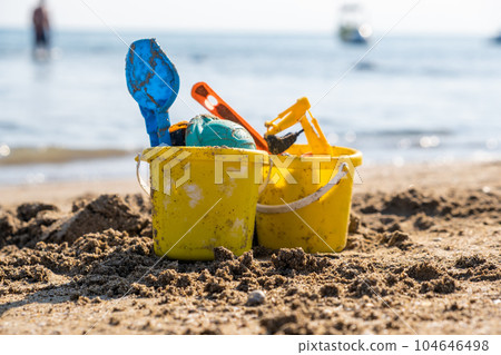 Children's beach toys - buckets, spade and shovel on sand on a sunny day. Bright toys on the background of the sea. 104646498