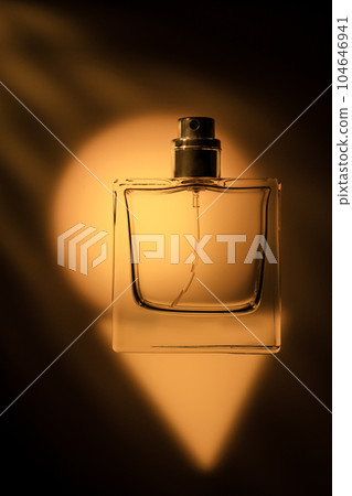Transparent perfume bottle on an orange background, beautiful shadows artistic photo. 104646941