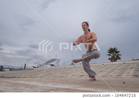 Caucasian man with naked torso practicing wushu on the seashore. Caucasian man with naked torso practicing wushu on the seashore. 104647218