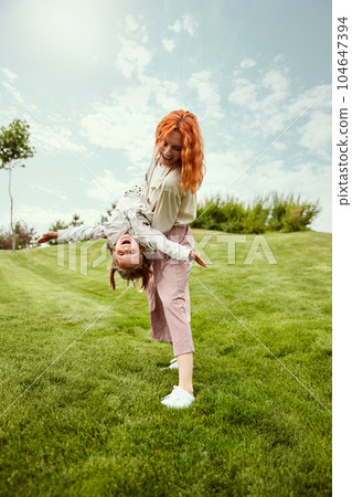 Joyful weekends. Beautiful redhead young woman, mother playing with her little daughter in the park on warm summer day 104647394