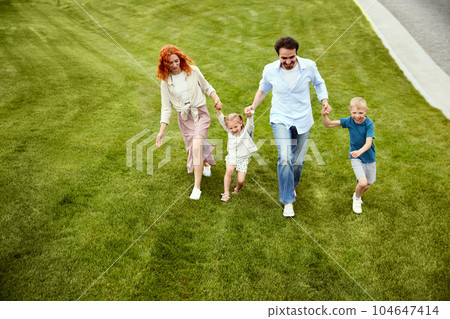 Young couple, man and woman going for a walk in park with their little children, boy and girl. Warm summer day walk Young couple, man and woman going for a walk in park with their little children, boy and girl. Warm summer day walk 104647414