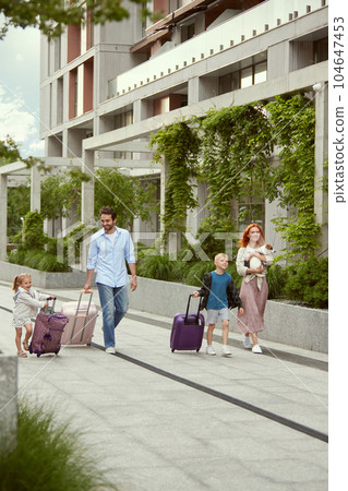Beautiful young couple, smiling man and woman going on summer vacation with little children and dog. People walking along street 104647453