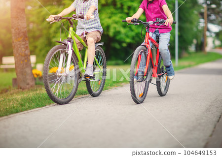 Two boys riding on their bicycles along an asphalt road 104649153