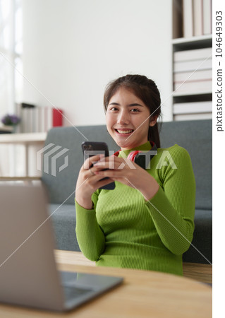 Young asian relaxed smiling pretty woman relaxing with mobile phone at home. Female feeling joy enjoying with mobile phone on cozy couch Young asian relaxed smiling pretty woman relaxing with mobile phone at home. Female feeling joy enjoying with mobile phone on cozy couch 104649303