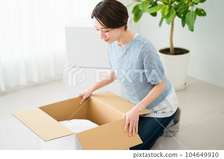 Young woman taking out luggage from cardboard Image of moving house Young woman taking out luggage from cardboard Image of moving house 104649910