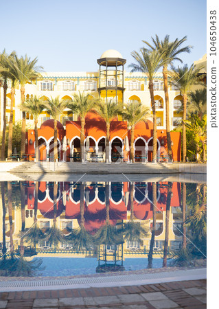 View of the pool, palm trees and the reflection of the sun on the castle grounds in Egypt - the concept of a luxury trip View of the pool, palm trees and the reflection of the sun on the castle grounds in Egypt - the concept of a luxury trip 104650438