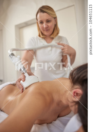 roller massage, Correction cellulite, FDA-approved. Young woman with body shaping machine, masseur massages client with vacuum roller, figure correction massage anti-cellulite massage roller massage, Correction cellulite, FDA-approved. Young woman with body shaping machine, masseur massages client with vacuum roller, figure correction massage anti-cellulite massage 104651115