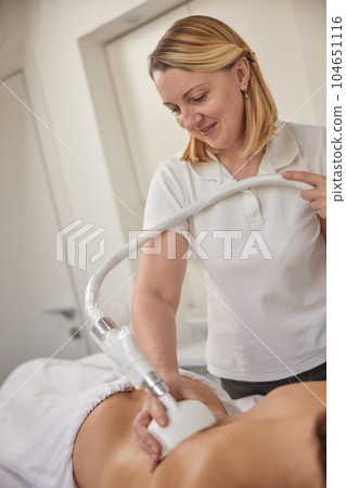 LPG massage, figure correction, anti cellulite. Young woman in beauty services, body shaping, masseur making vacuum roller massage on client, figure correction, anti cellulite massage LPG massage, figure correction, anti cellulite. Young woman in beauty services, body shaping, masseur making vacuum roller massage on client, figure correction, anti cellulite massage 104651116