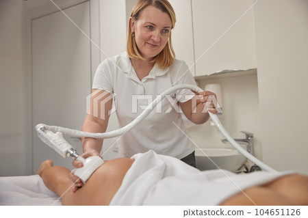 holding massager, massage procedure, weight loss. Attractive young woman is participating in beauty services, body shaping, vacuum roller massages. Offering clients figure correction massages holding massager, massage procedure, weight loss. Attractive young woman is participating in beauty services, body shaping, vacuum roller massages. Offering clients figure correction massages 104651126