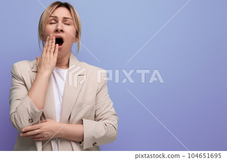 sleepy tired blond business young woman in jacket yawns on studio background 104651695