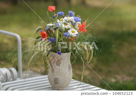 Wild flower bouquet (Cornflowers, chamomiles wheat and poppies) in terracotta vase. Wildflower and grass varieties. Wild flower bouquet (Cornflowers, chamomiles wheat and poppies) in terracotta vase. Wildflower and grass varieties. 104652123