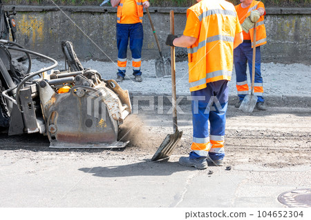 A road tractor with a powerful mounted mill removes a layer of old asphalt on the roadway. A road tractor with a powerful mounted mill removes a layer of old asphalt on the roadway. 104652304