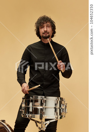 Stylish man, talented musician playing drums against light brown studio background. Lovely sounds Stylish man, talented musician playing drums against light brown studio background. Lovely sounds 104652350