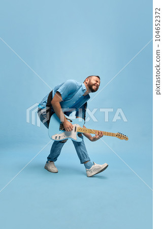 Artistic, expressive, talented man, musician in casual clothes playing electric guitar against blue studio background Artistic, expressive, talented man, musician in casual clothes playing electric guitar against blue studio background 104652372