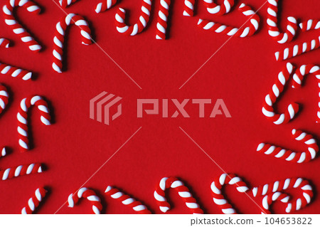 Flat lay Christmas composition with frame of candy canes on a red background. Copy space for text 104653822