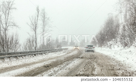 Cars driving on snow covered forest road during snowstorm, fog in disance, view from car behind. Dangerous driving conditions. Cars driving on snow covered forest road during snowstorm, fog in disance, view from car behind. Dangerous driving conditions. 104655532
