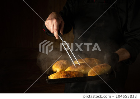 Baking delicious pies for a festive dinner. A baking sheet in the chef hand with freshly baked buns and fork. Copy space Baking delicious pies for a festive dinner. A baking sheet in the chef hand with freshly baked buns and fork. Copy space 104655838