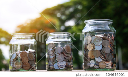 Coins in glass jar with blurred green trees background, concept of money savings       104656001