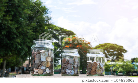 Coins in glass jar with blurred green trees background, concept of money savings       104656002