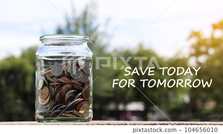 Coins in glass jar with the text save to day for tomorrow with blurred green trees background, concept of money savings                               104656010