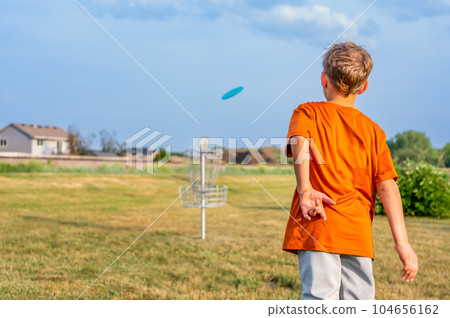 Young Caucasian male boy aiming a disc golf at a chain goal.  104656162