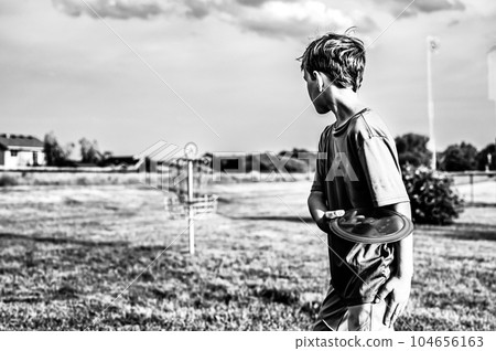 Young Caucasian male boy aiming a disc golf at a chain goal.  Young Caucasian male boy aiming a disc golf at a chain goal.  104656163