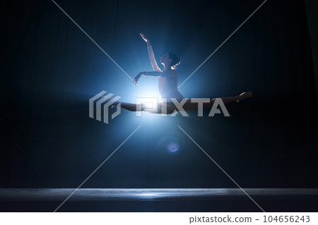 Elegant femininity. Beautiful, tender young woman, ballerina dancing against dark blue background with spotlight Elegant femininity. Beautiful, tender young woman, ballerina dancing against dark blue background with spotlight 104656243
