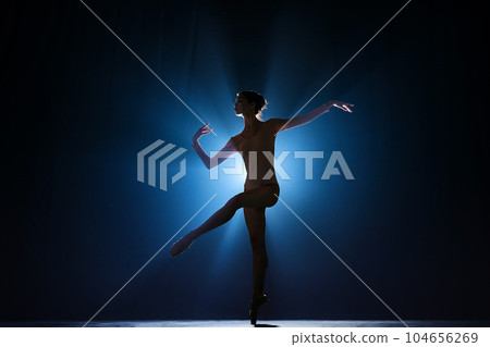 Attractive, artistic, talented young girl, ballerina dancing classical dance, performing against dark blue background with spotlight 104656269