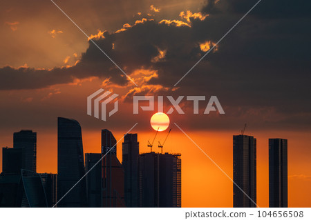 The setting sun over the skyscrapers of the Moscow City office center on a summer evening. Sunset. The setting sun over the skyscrapers of the Moscow City office center on a summer evening. Sunset. 104656508