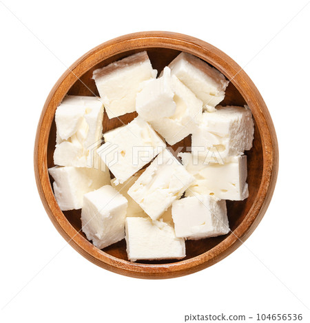 Greek feta cubes, brined cheese cut in block shape, in a wooden bowl. Cheese, matured in brine, with a soft and moist texture, and with fresh, salty and acidic taste. Isolated, from above, food photo. 104656536