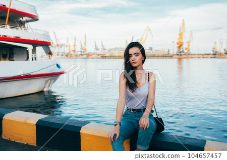Girl with long brown hair sitting in seaport looking at the camera 104657457