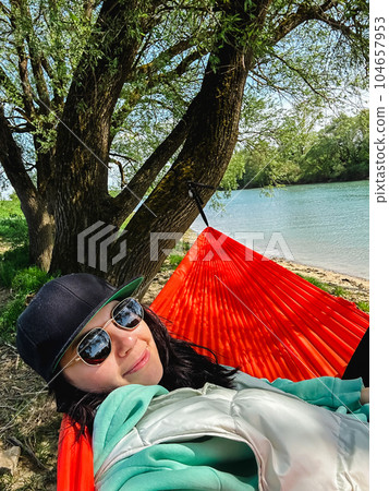 A woman in a cap rests in a hammock overlooking the river A woman in a cap rests in a hammock overlooking the river 104657953