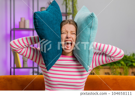 Repair work at neighbours concept, irritated woman at home cover ears with pillows annoyed by noise 104658111