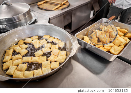 Male cook preparing delicious National Kazakh pastries baursak. street cafe. Fry dough in boiling oil in a frying pan. Male cook preparing delicious National Kazakh pastries baursak. street cafe. Fry dough in boiling oil in a frying pan. 104658185