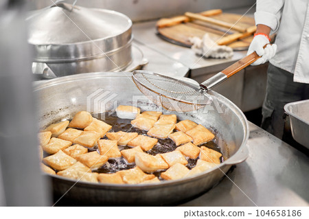 Male cook preparing delicious National Kazakh pastries baursak. street cafe. Fry dough in boiling oil in a frying pan. Male cook preparing delicious National Kazakh pastries baursak. street cafe. Fry dough in boiling oil in a frying pan. 104658186