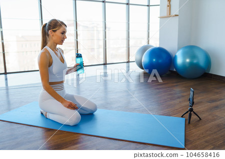 Young Woman on Yoga Mat Filming Online Workout with Phone 104658416