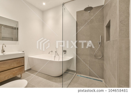 a bathroom with a tub, sink and toilet in the background is a mirror on the wall next to the bathtub a bathroom with a tub, sink and toilet in the background is a mirror on the wall next to the bathtub 104658481
