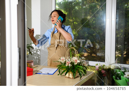 Pregnant woman flower designer talks on mobile phone, receives order for flower arrangement in floral design studio 104658785