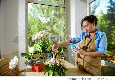 Pregnant woman florist, flower designer takes a photo of a cute floral arrangement on smartphone in floral design studio Pregnant woman florist, flower designer takes a photo of a cute floral arrangement on smartphone in floral design studio 104658799