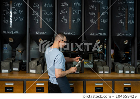 Barista roasting shop worker standing at counter pouring coffee beans. 104659429