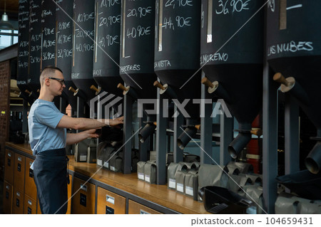 Coffee shop worker standing at counter pouring coffee beans. Coffee shop worker standing at counter pouring coffee beans. 104659431