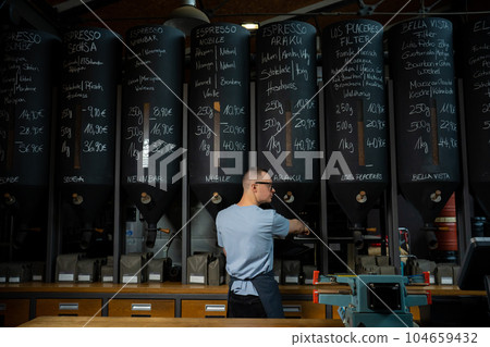 Barista roasting shop worker standing at counter pouring coffee beans. Barista roasting shop worker standing at counter pouring coffee beans. 104659432