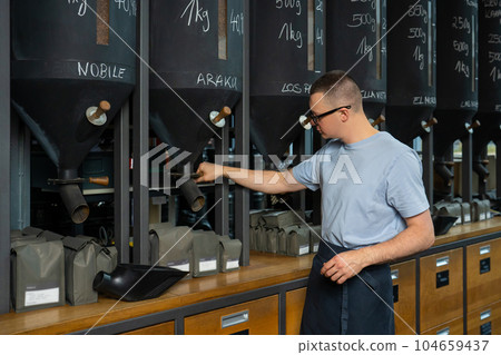 Coffeemaker barista standing at counter pouring coffee beans. 104659437